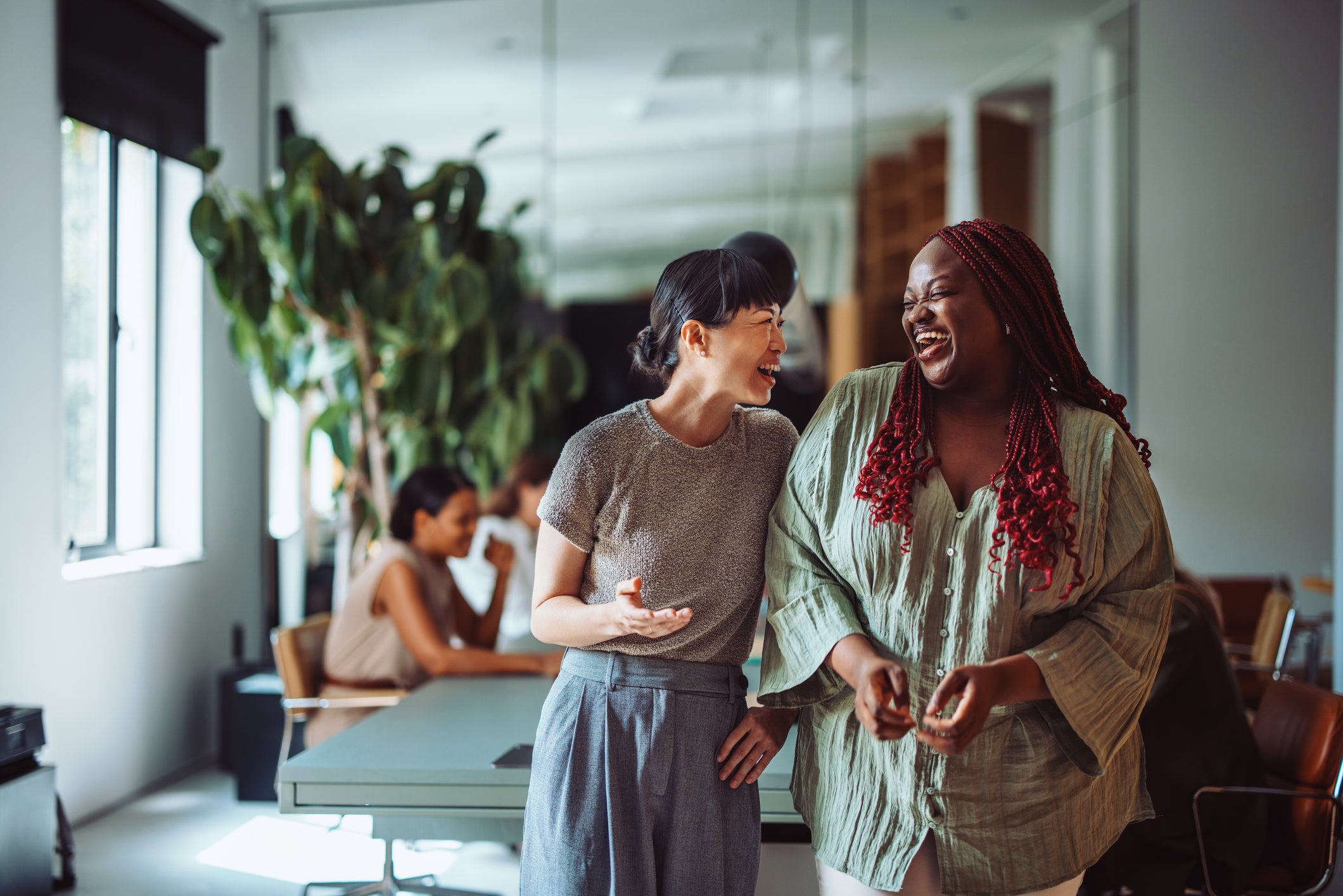 Two coworkers sharing a joyful moment and laughing together during a break in a modern office environment.